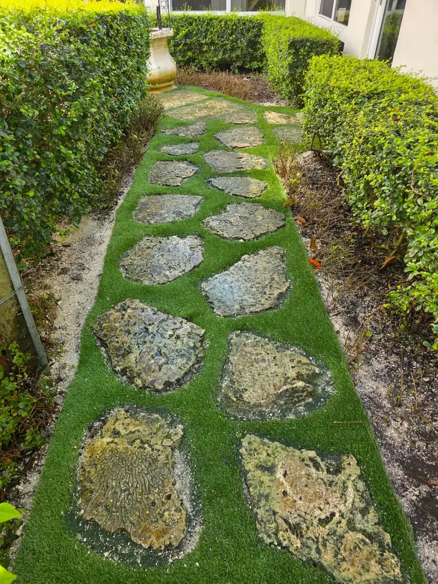 Roll of fresh sod being laid on prepared soil next to a stone wall