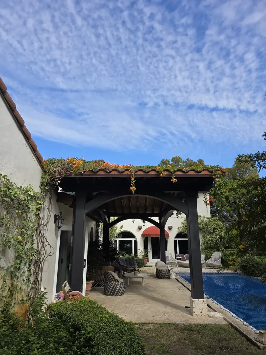 Black aluminum louvered pergola over a patio with turf and a green wall